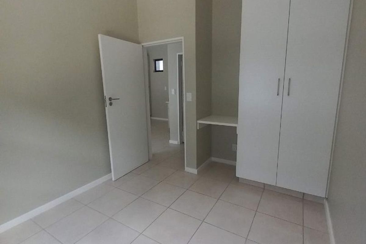 A clean, empty bedroom featuring neutral tiled flooring, a built-in wardrobe, and a small integrated desk area.