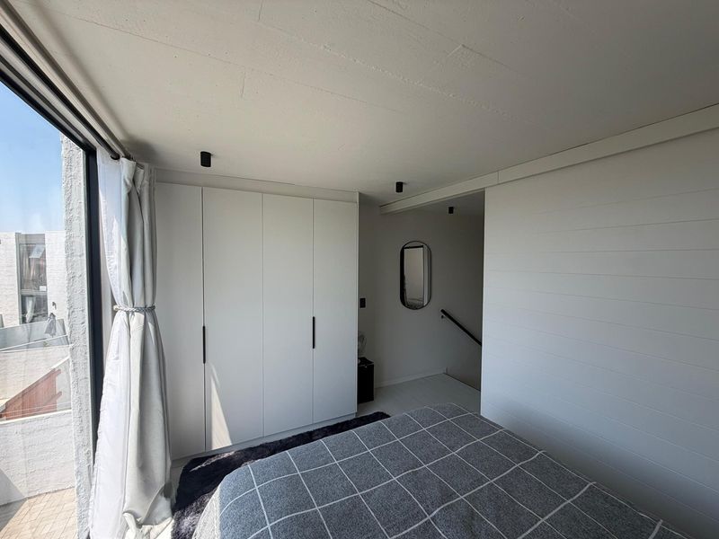 A modern bedroom featuring built-in wardrobes, sleek plank-style wall paneling, recessed ceiling lighting, and a large sliding glass door leading to an outdoor area.