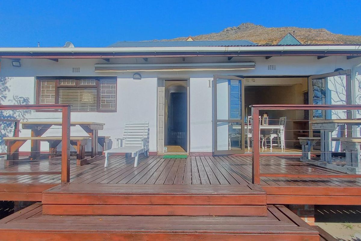Rear view of the property featuring a spacious timber deck with balustrades, providing direct access to the interior through sliding glass doors.