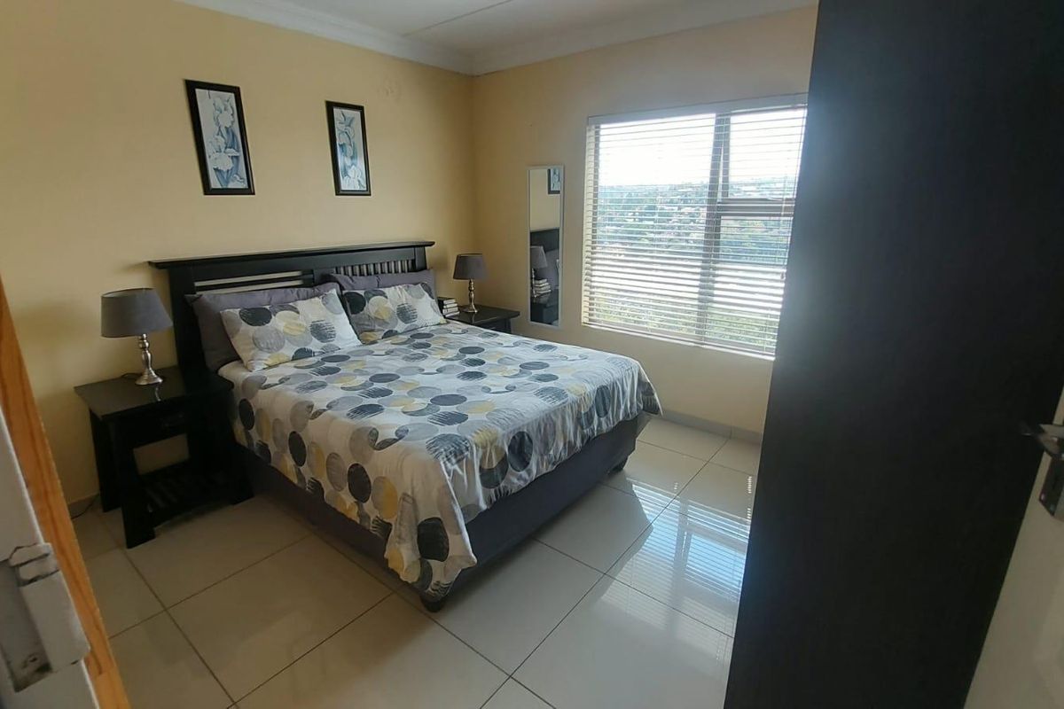 A well-lit bedroom featuring large format floor tiles, a window with fitted blinds, and neutral wall finishes.