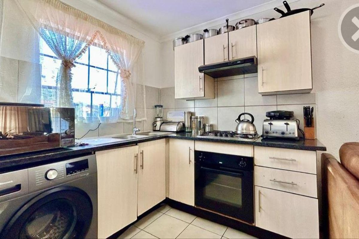 Compact kitchen featuring light-toned cabinetry, built-in oven, gas hob, extractor fan, and integrated space for a washing machine.