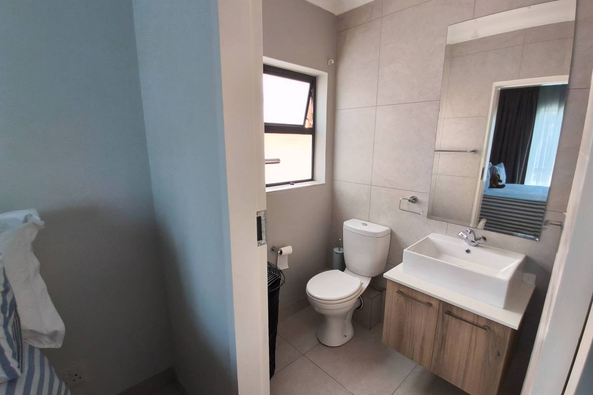 A modern bathroom featuring a wall-mounted vanity with a vessel sink, a toilet, and large-format neutral wall tiles.