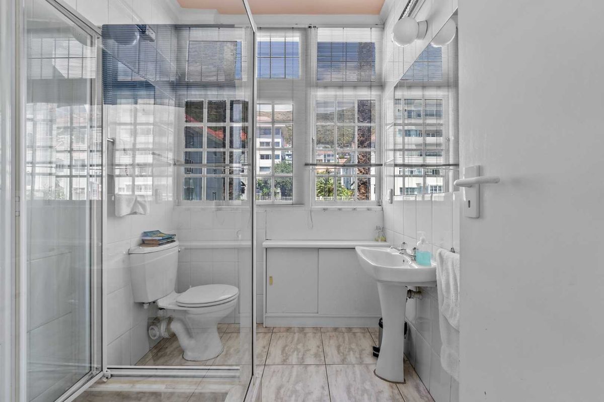 A functional bathroom featuring a pedestal basin, toilet, and a glass-enclosed shower, finished with tiled walls and flooring.