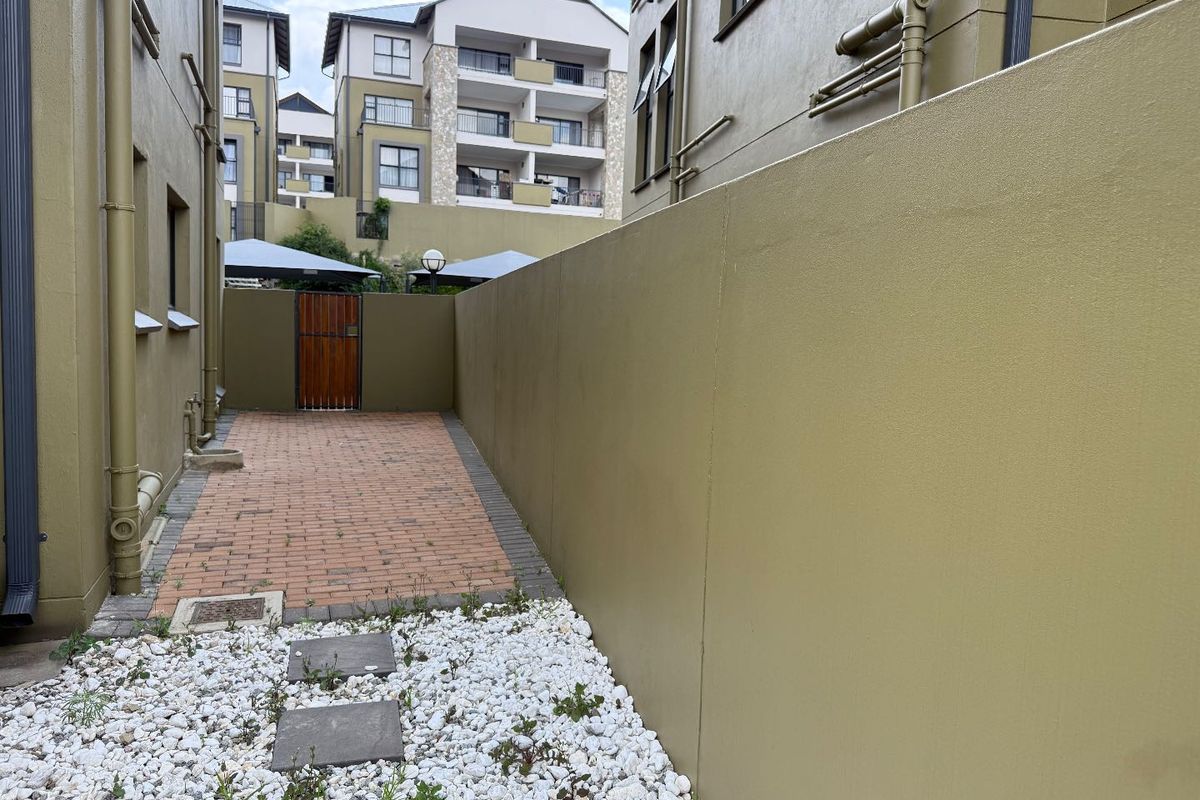 A side exterior walkway featuring paved brick pathways, decorative white gravel, and a high boundary wall between apartment blocks.