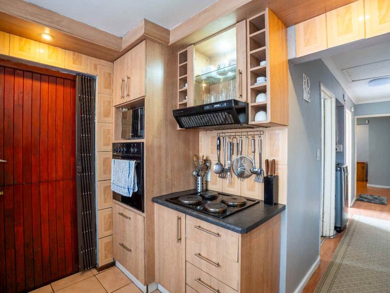 Compact kitchen featuring wood-finish cabinetry, built-in oven, electric hob, extractor fan, and tiled splashback, leading into a hallway.