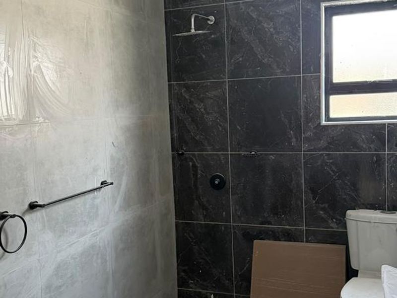 A bathroom currently under renovation featuring dark and light tiled walls, a modern shower fixture, and a standard toilet.