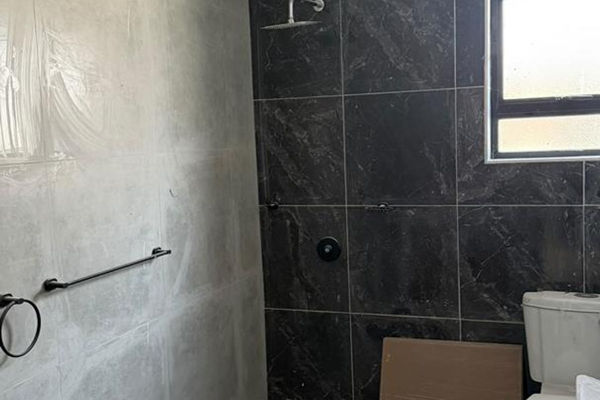 A bathroom currently under renovation featuring dark and light tiled walls, a modern shower fixture, and a standard toilet.