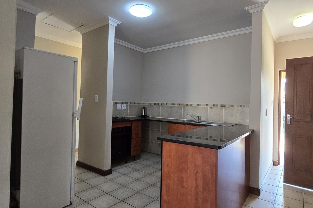 A functional kitchen featuring granite countertops, built-in wooden cabinetry, tiled flooring, and a breakfast bar, offering a clean and practical layout.