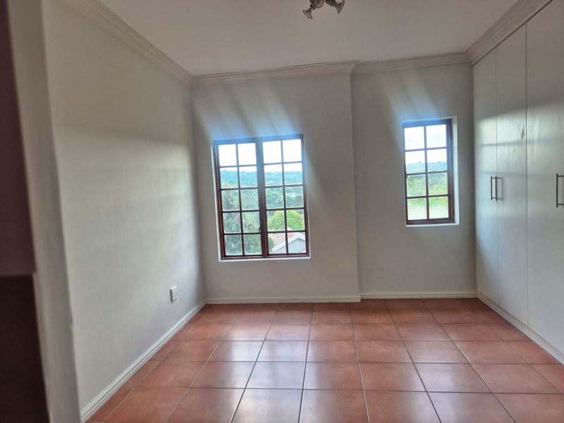 An empty bedroom featuring tiled flooring, built-in cupboards, and wooden window frames with natural light.