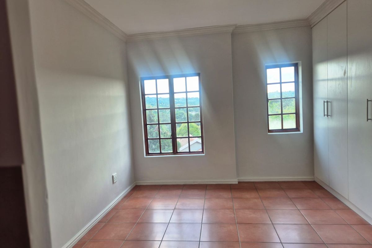 An empty bedroom featuring tiled flooring, built-in cupboards, and wooden window frames with natural light.