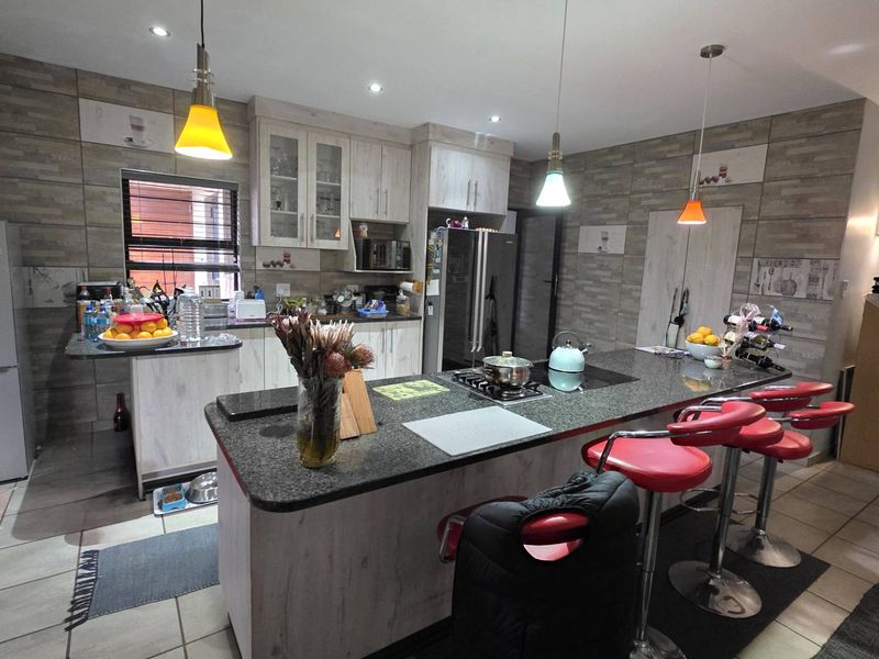 Spacious kitchen featuring a large central island with granite countertops, built-in cabinetry, and modern pendant lighting, offering a functional and contemporary cooking space.