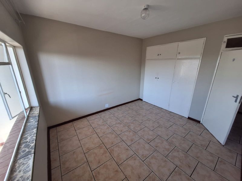 An empty bedroom featuring tiled flooring, built-in cupboards, and a window with a stone-look sill.
