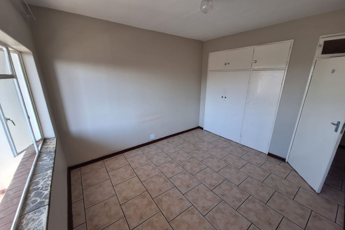 An empty bedroom featuring tiled flooring, built-in cupboards, and a window with a stone-look sill.