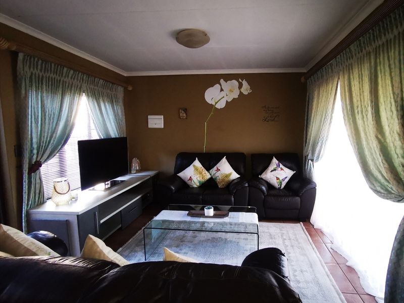 A comfortable living room featuring tiled flooring and large windows with curtain rails, providing a functional and well-lit space for relaxation.