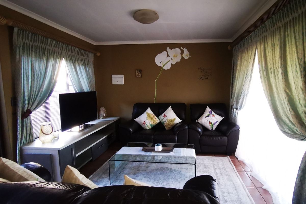A comfortable living room featuring tiled flooring and large windows with curtain rails, providing a functional and well-lit space for relaxation.