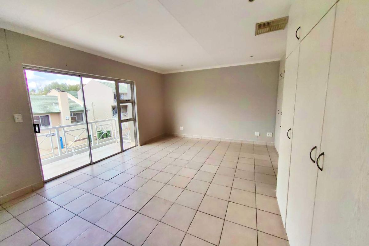 Spacious, empty bedroom featuring neutral tiled flooring, extensive built-in cupboards, and a sliding glass door providing direct access to a private balcony.