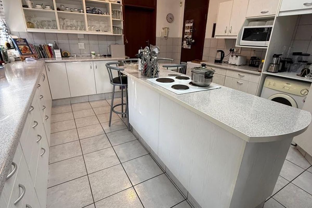 Functional kitchen featuring white cabinetry, a central island with a built-in electric hob, tiled flooring, and ample storage space.