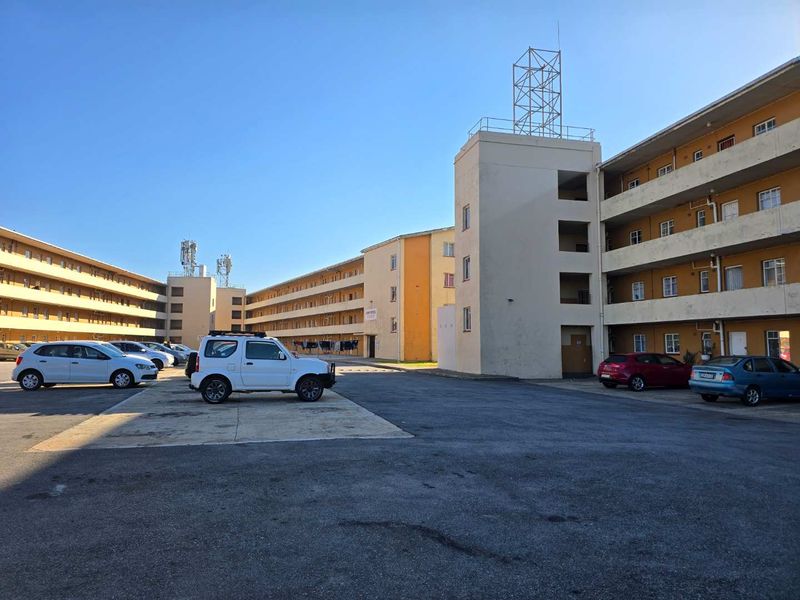 Exterior view of a multi-story apartment complex featuring a large asphalt parking courtyard and functional stairwell towers.