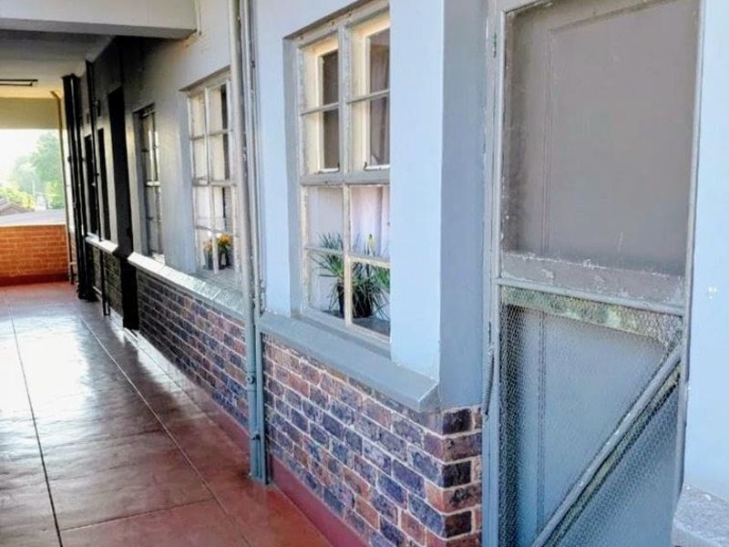 An exterior apartment hallway featuring brick accents, tiled flooring, and traditional casement windows with a screen door entrance.