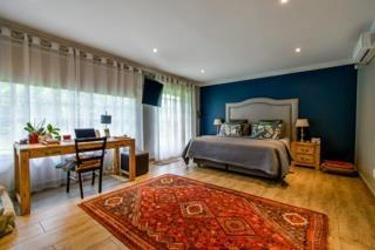 Spacious bedroom featuring wood-look flooring, recessed ceiling lighting, and a large window with sheer curtains, creating a bright and comfortable living space.