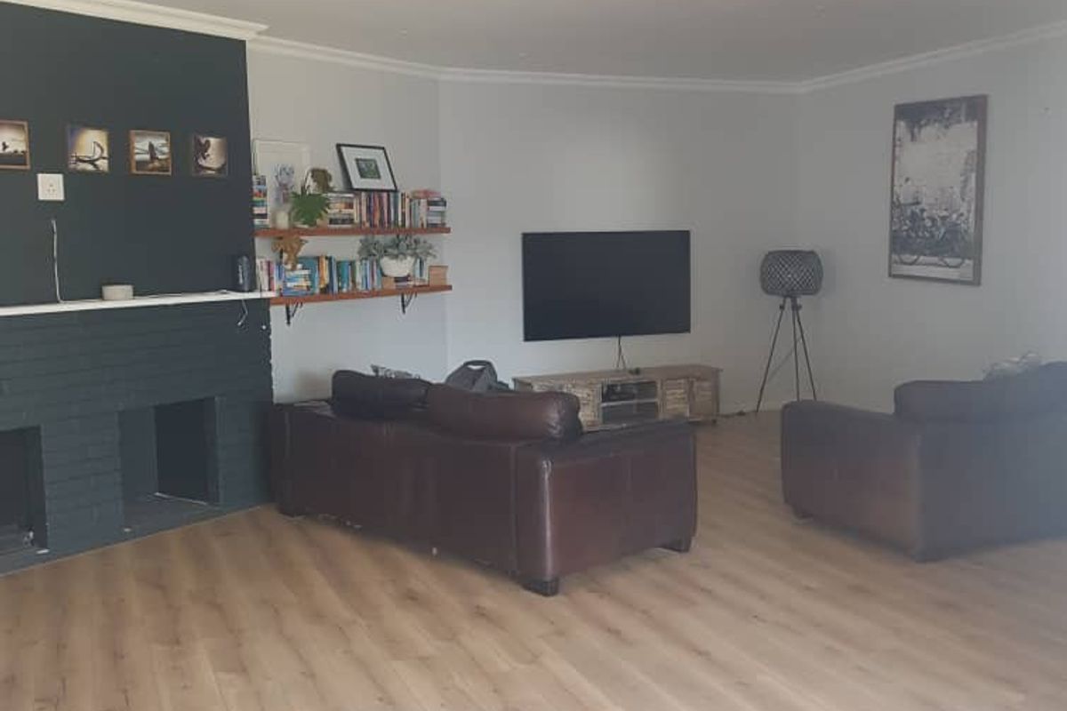 Spacious living room featuring light wood-look laminate flooring and a dark painted brick fireplace feature wall.