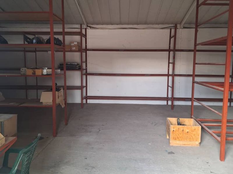 A functional industrial utility or storage space featuring concrete flooring, a pitched metal roof, and extensive built-in metal shelving units.