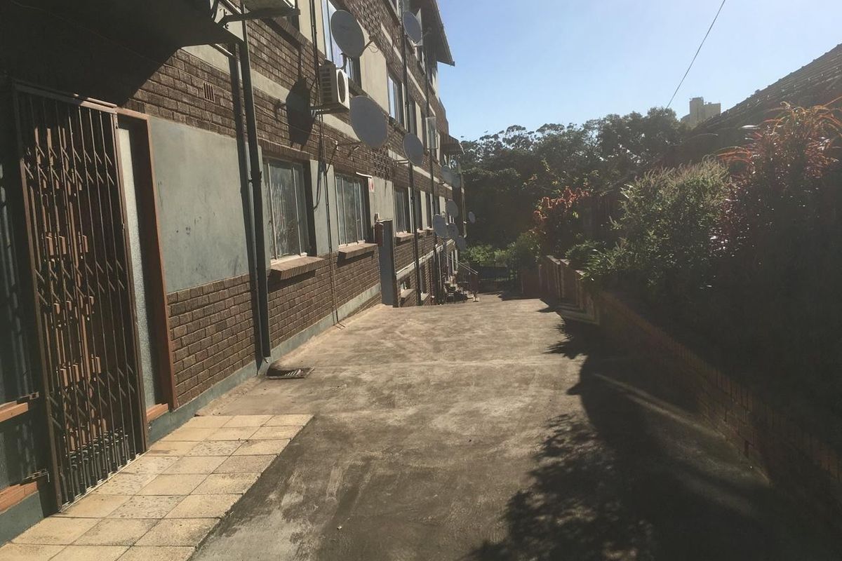 Rear exterior view of the apartment building featuring a concrete driveway, brick facade, and security gate access.