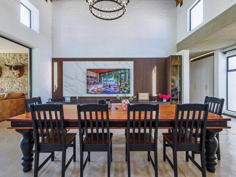 Spacious open-plan living and dining area featuring high vaulted ceilings, exposed brick walls, polished concrete floors, and a modern feature wall with integrated lighting.