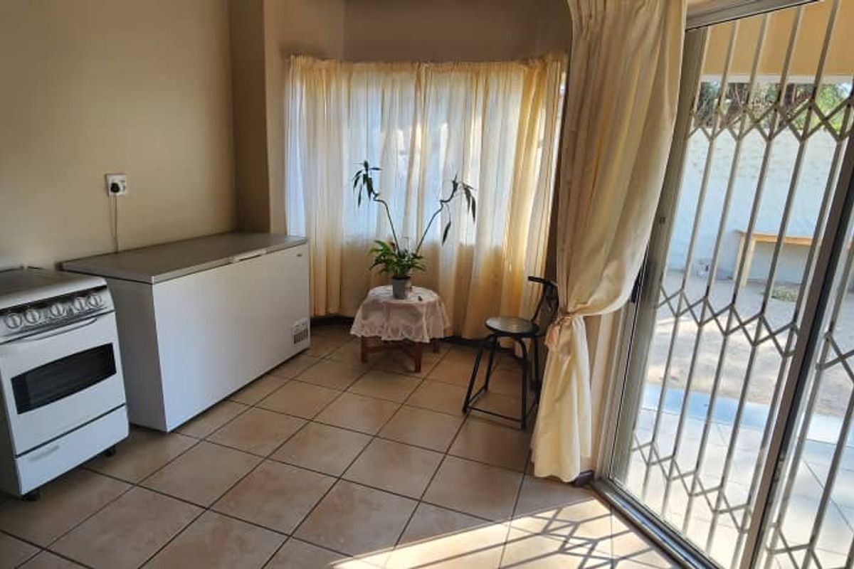 A functional kitchen area featuring tiled flooring, a freestanding stove, and sliding glass doors with security gates leading to an outdoor patio space.