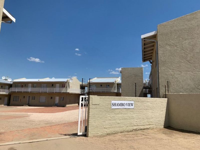 Front entrance view of Shambo View townhouse complex featuring a gated access point, paved driveway, and multi-unit residential buildings with balconies.