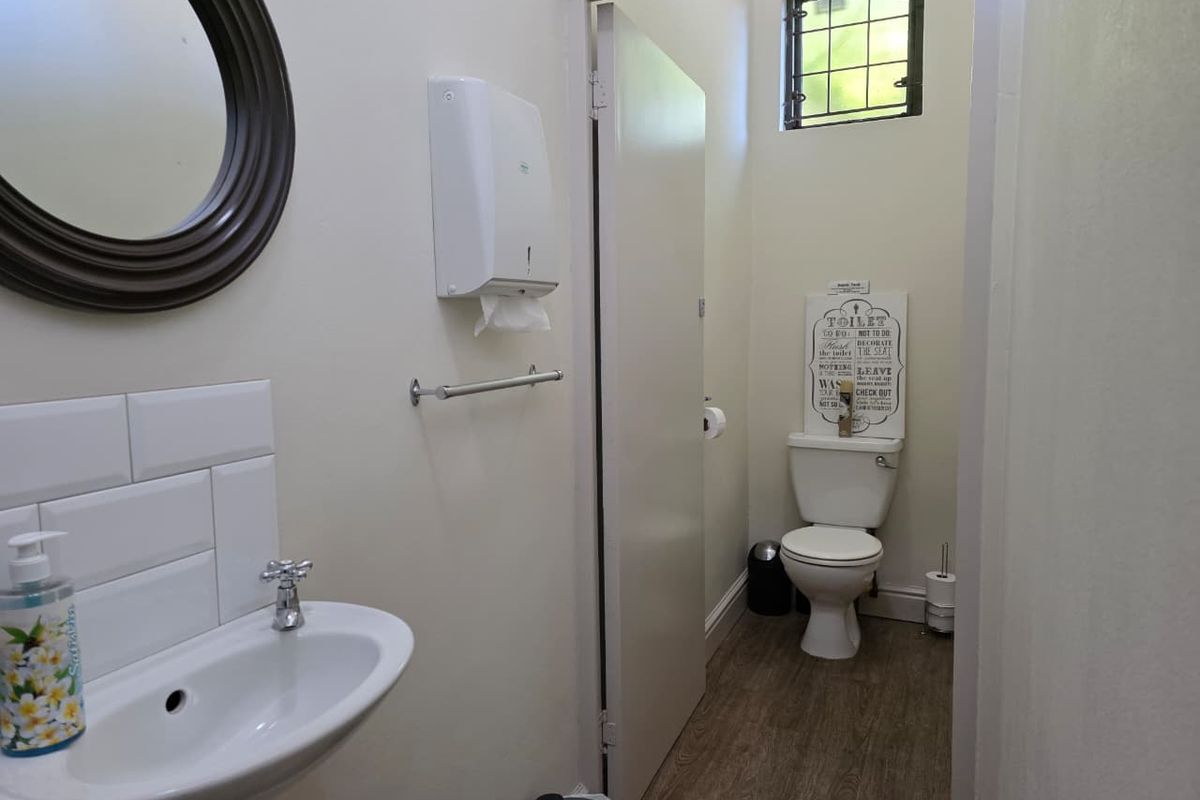 A functional bathroom featuring a pedestal basin with tiled splashback and a separate toilet area with a small window and security bars.