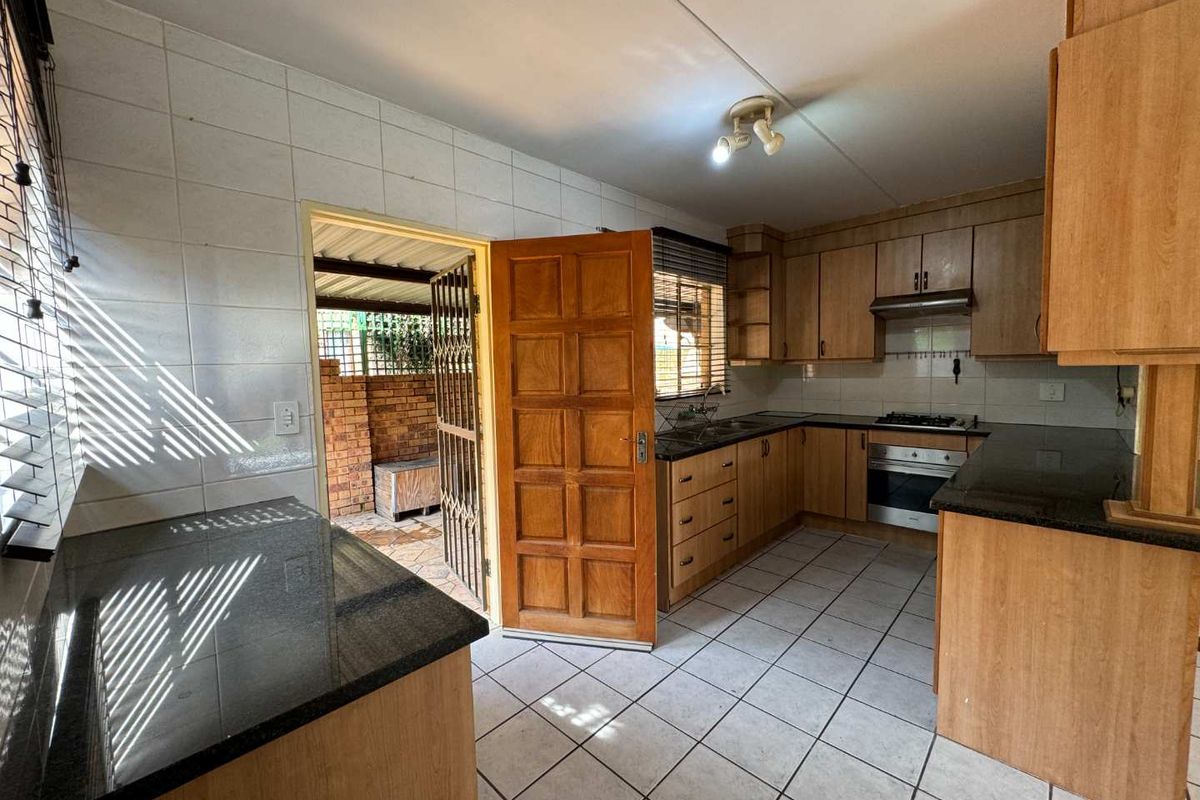 Functional kitchen featuring granite countertops, built-in wooden cabinetry, integrated oven and hob, with direct access to an outdoor area.