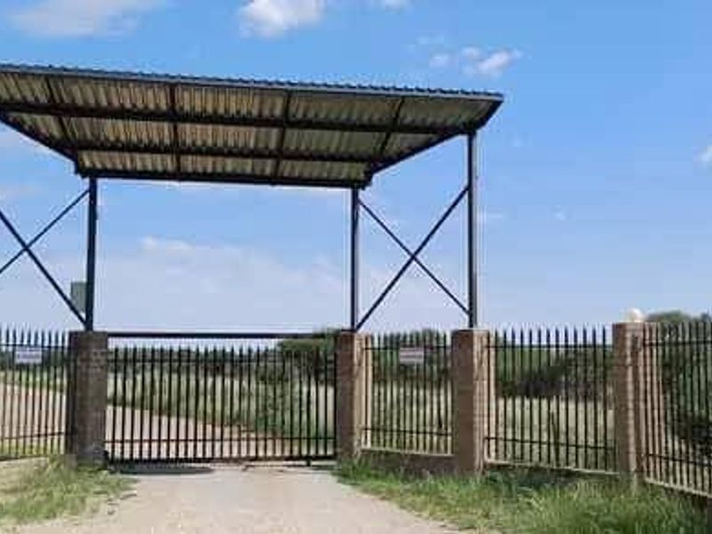A secure gated entrance to the vacant residential property featuring brick pillars, metal fencing, and a covered overhead structure.