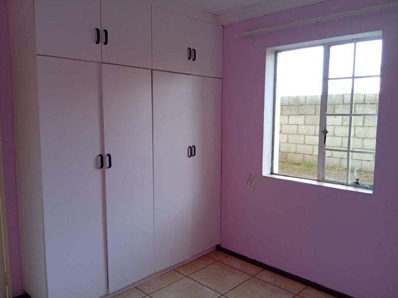 A vacant bedroom featuring built-in cupboards, tiled flooring, and a steel-framed window, requiring minor cosmetic repairs to the wall plaster.