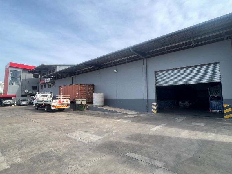 Exterior view of a commercial warehouse facility featuring a large concrete yard, metal cladding, and a roller shutter door for loading access.
