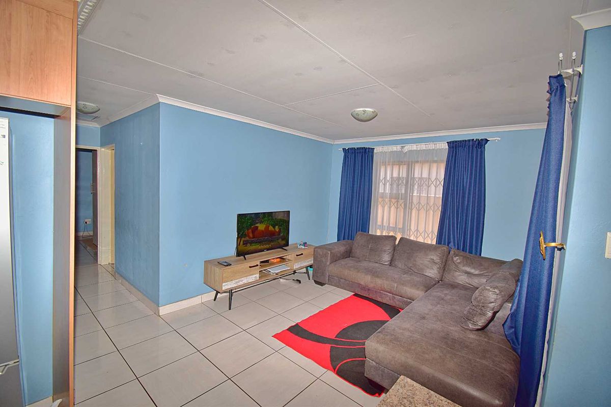 A living room featuring tiled flooring, blue painted walls, and a window with security bars, providing a functional and accessible living space.