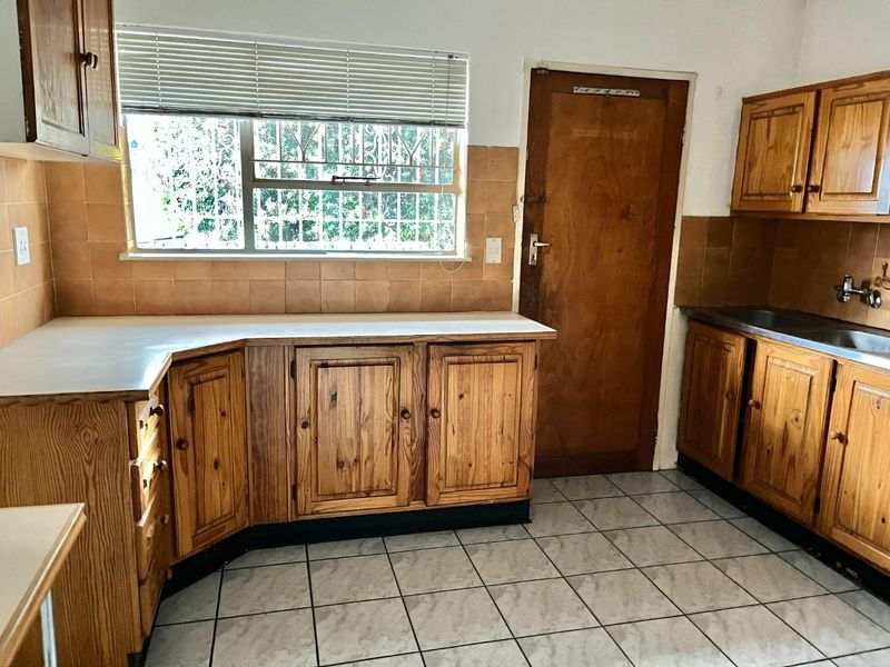 A functional kitchen featuring wooden cabinetry, laminate countertops, tiled backsplash, and tiled flooring, offering a blank canvas for potential modernization and renovation.