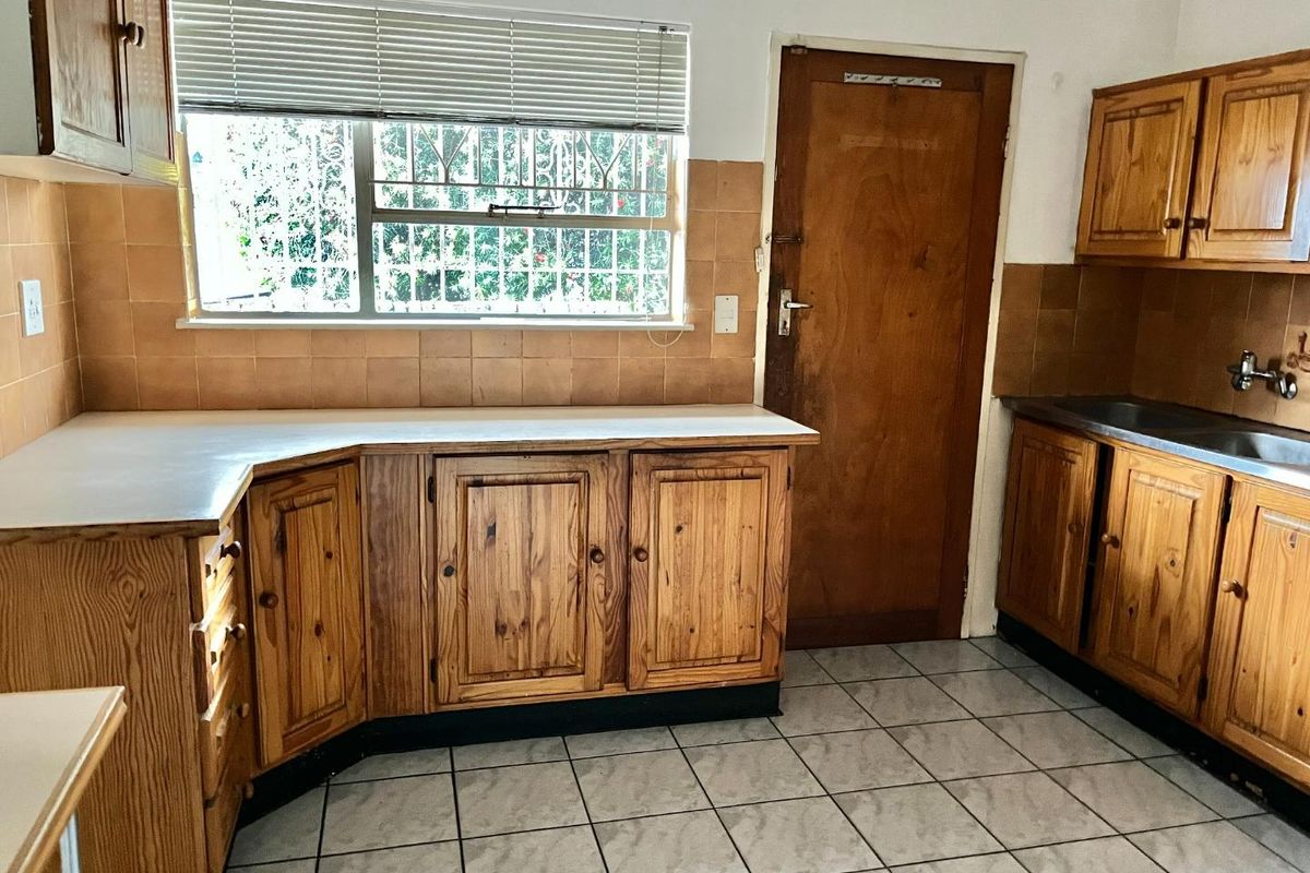 A functional kitchen featuring wooden cabinetry, laminate countertops, tiled backsplash, and tiled flooring, offering a blank canvas for potential modernization and renovation.