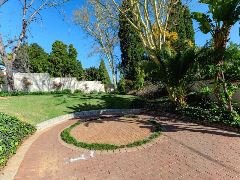 A well-maintained garden featuring a circular paved patio area, lush lawn, and established perimeter boundary walls.