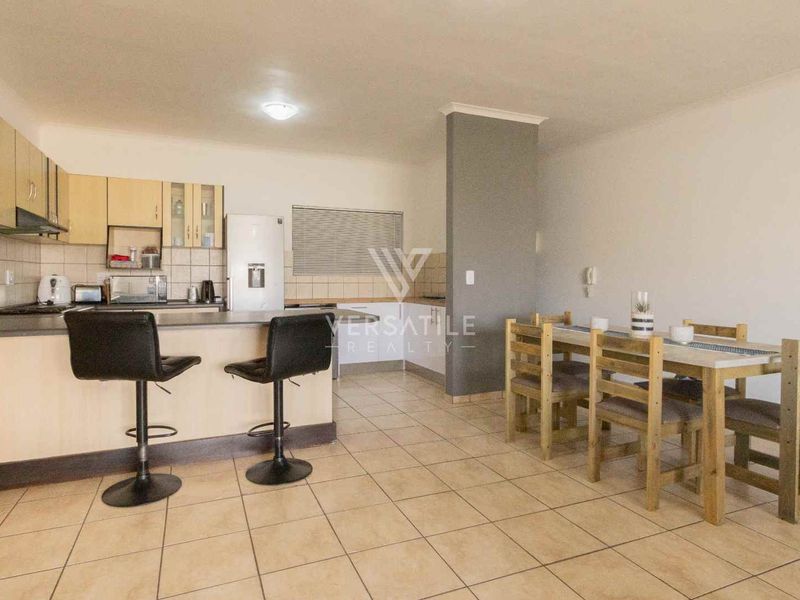 Open-plan kitchen and dining area featuring tiled flooring, built-in cabinetry, and a breakfast bar, offering a functional layout for modern living.