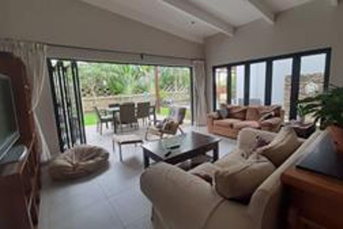 Spacious living room featuring exposed ceiling beams and large bi-fold doors that open onto an outdoor patio area.