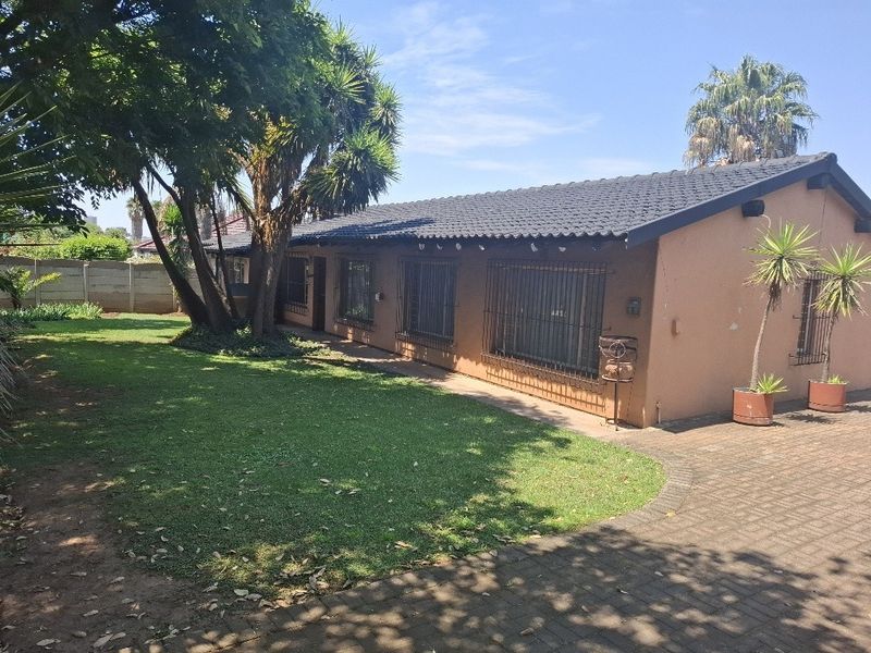 Rear view of the house featuring a tiled roof, security bars on windows, paved driveway, and a well-maintained lawn area.