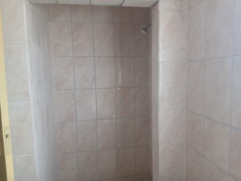 A basic shower enclosure featuring neutral ceramic wall tiles and a fixed shower head.