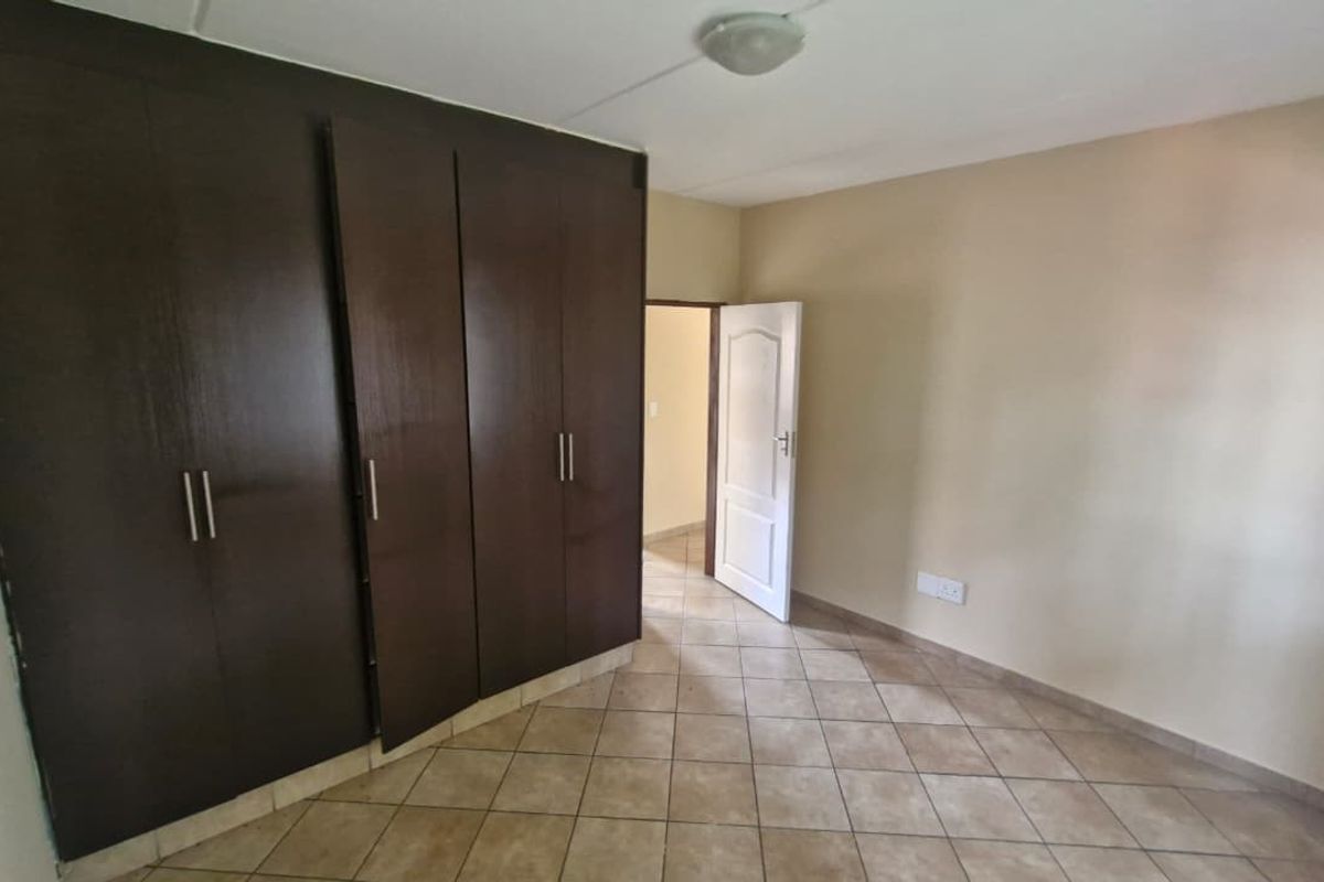 A bedroom featuring dark wood built-in cupboards, tiled flooring, and a neutral color palette, offering a functional and clean living space.