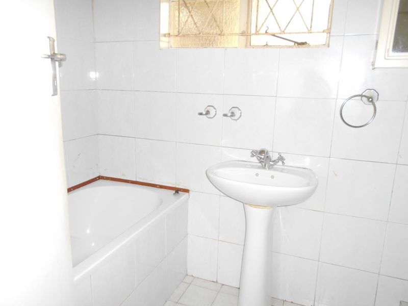A functional bathroom featuring a pedestal basin, bathtub, and fully tiled walls, requiring cosmetic updates to improve its overall condition and aesthetic appeal.