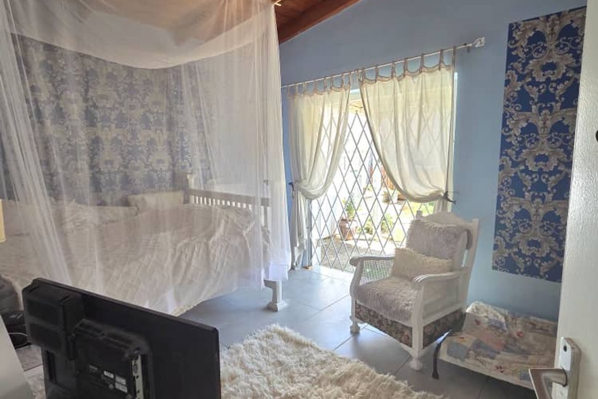 A bedroom featuring exposed timber ceiling beams, tiled flooring, and a sliding door with security gate leading to the exterior.