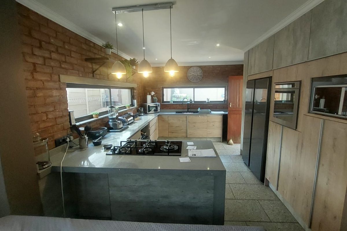 Modern kitchen featuring a central island with a built-in gas hob, exposed brick feature wall, stone countertops, and integrated cabinetry.