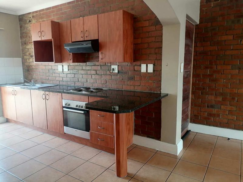 Kitchen featuring wooden cabinetry, granite countertops, built-in oven and hob, and an exposed brick feature wall with tiled flooring.
