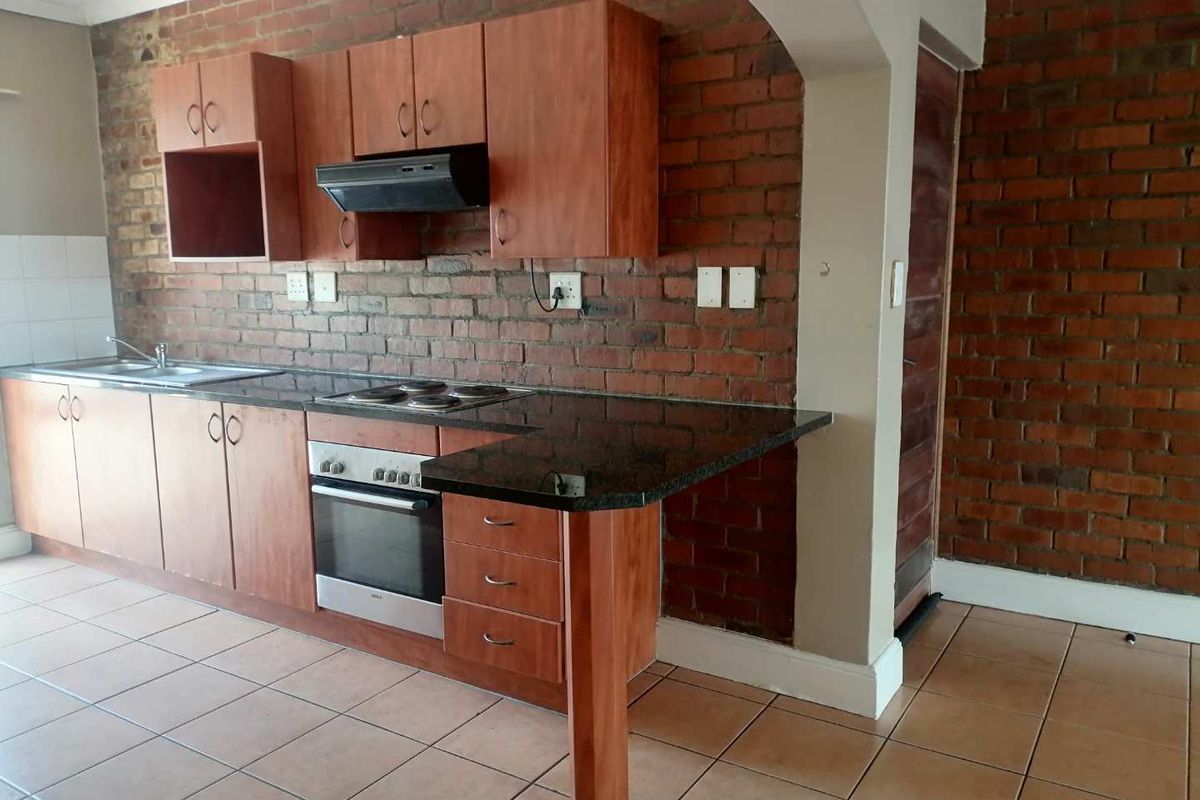 Kitchen featuring wooden cabinetry, granite countertops, built-in oven and hob, and an exposed brick feature wall with tiled flooring.
