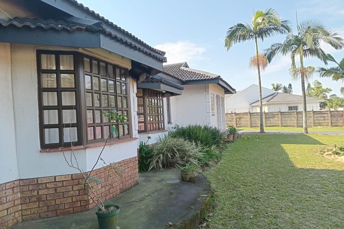 Rear view of the house featuring a concrete patio, brick base detailing, and large grid-style windows overlooking a spacious garden area.